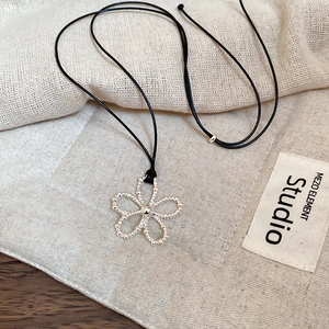 Détail macro du pendentif fleur argentée ajourée sur cordon en cire noire réglable
