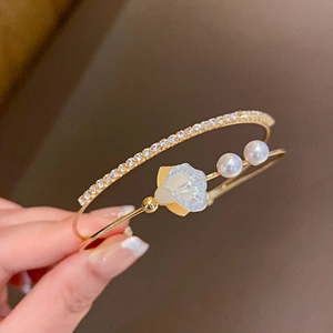 Detailed close-up of a layered gold bracelet with white pearls, floral charm and sparkling diamonds