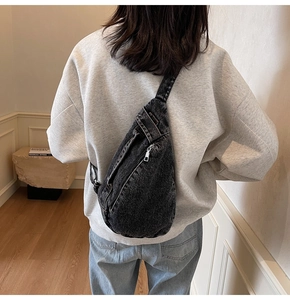 Detail of a dark gray washed denim crossbody bag worn over the shoulder on a model