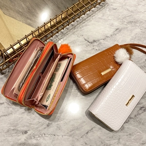 Three crocodile pattern wallets in orange, brown, and white with card slots and fur pompom