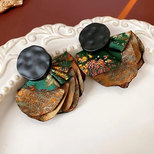 Detailed macro view of silk fabric fan earrings with gold patterns on a white plate