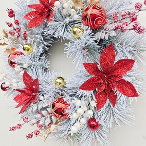 Christmas wreath with red poinsettia, gold ornaments, white berries and flocked pine branches