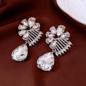 Close-up of silver drop earrings with star and pearl zircon stones on red satin