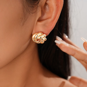 Close-up of a high-shine golden twisted knot earring worn by a female model