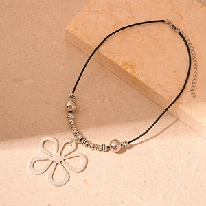 Silver hollow flower pendant necklace with black woven rope on a textured stone background