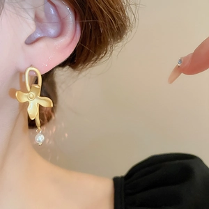 Close-up of model wearing matte gold flower earrings with elegant drop pearl detail
