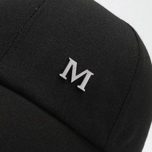 Black twill canvas baseball cap with silver metal 'M' logo on a grey background