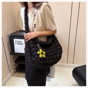 Detail of black quilted cloud bag with plush flower charm and wide shoulder strap