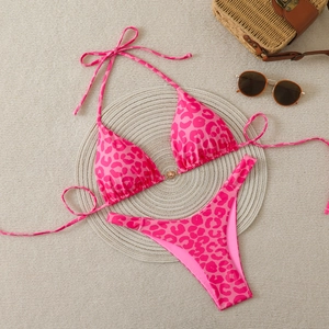 Flat lay of pink leopard print bikini set with gold sun hardware and vacation accessories