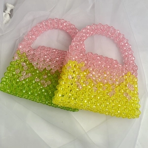 Detail of pink, green and yellow handmade beaded purses on white fabric surface