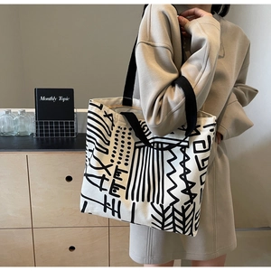 Close-up of cream canvas tote bag with black abstract graffiti and wide shoulder strap