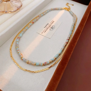 Macro view of blue marbled bead and gold H-link double-layer necklace in a jewelry box