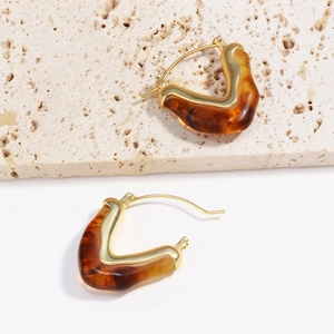 Dettaglio macro di orecchini geometrici in resina dorata con trama a tartaruga marrone