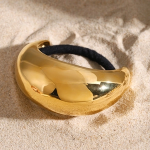 Gold stainless steel hair tie with black elastic band on beach sand, minimalist style