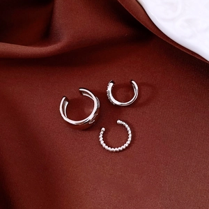 Detail showing a three-piece set of silver ear cuffs with zircons on red silk fabric
