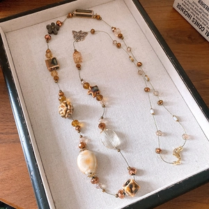 Detail of beaded necklace with ceramic flowers and metal butterfly on jewelry tray