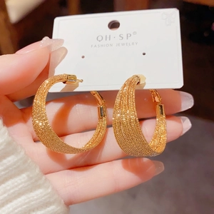 Detailed close-up of woven gold hoop earrings featuring multi-strand metallic chains