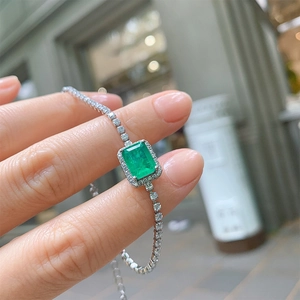 Elegant silver bracelet with rectangular emerald gemstone and diamond halo on model wrist