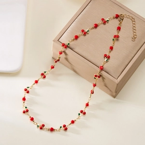 Close-up of red cherry bead necklace with green leaves on a beige jewelry display box