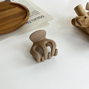 Detailed close-up of matte khaki hair claw clip on a minimalist wooden tray display