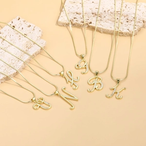 Detail view of gold snake chains with zircon-inlaid letter pendants on textured stone