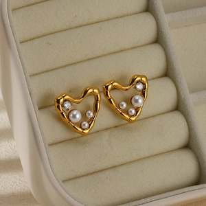 Macro detail of gold heart earrings featuring pearls and zircon on a velvet tray