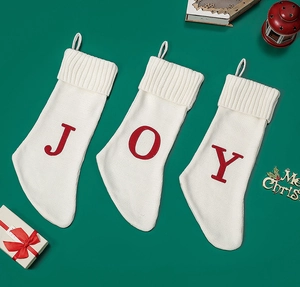 Detailed view of three white knitted Christmas stockings with red JOY letter patterns