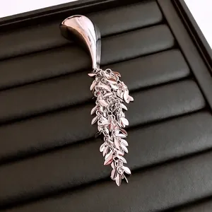 Geometric silver metal brooch with cascading leaf fringe on black textured display