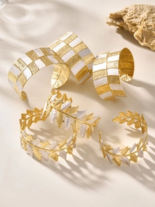 Dettaglio di bracciali artistici in metallo oro e bianco con corona di foglie e griglia