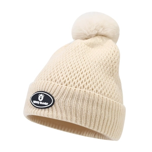 Close-up of beige knit beanie with a fluffy pom-pom and a cute Teddy Island logo patch