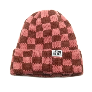 Detail view of the thick checkered knit fabric and the white brand label on the pink beanie