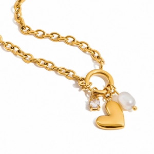 Detail of gold chain necklace featuring heart charm, cubic zirconia, and pearl pendant