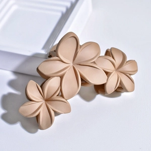 Macro detail of three matte beige flower hair claws on a clean white geometric tray