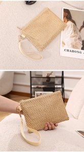 Detail of woven straw clutch bag with a gold metal zipper and cream wristlet strap