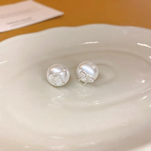 Detail of elegant bow knot pearl stud earrings on a white ceramic display plate