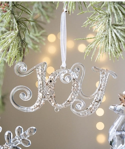 Close-up of JOY shaped clear acrylic Christmas ornament with gold sequins on a tree branch