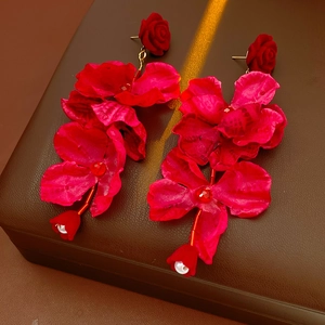 Vue détaillée de boucles d'oreilles fleurs en tissu rouge avec perles sur boîte en cuir
