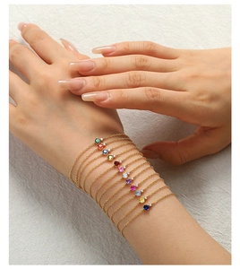 Detail of stacked gold bracelets featuring vibrant round colorful zircon stones on a wrist