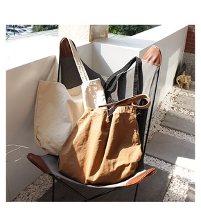 Three oversized canvas tote bags in beige, black, and brown colors on a butterfly chair