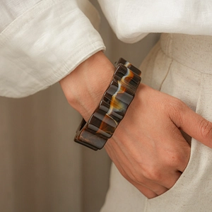 Close-up of a wide wavy tortoiseshell acrylic bangle worn on a wrist in natural lighting