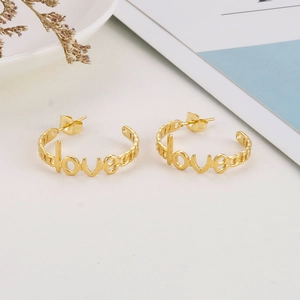 Macro detail of golden stainless steel LOVE letter hoop earrings on a white surface
