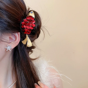 Detailed close-up of a fish-shaped hair clip with red sequins and a snowflake pearl earring