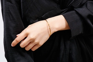 Detail of minimalist gold-finish bangle featuring small ball accents on a model wrist