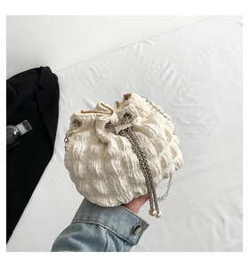 Detail of white pleated bucket bag with silver chain strap and pearl tassel accessory