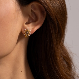 Close-up of vintage gold stud earring with central gem and pearl border on model