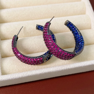 Macro detail of C-shaped hoop earrings with pink and blue zircons in a velvet jewelry box