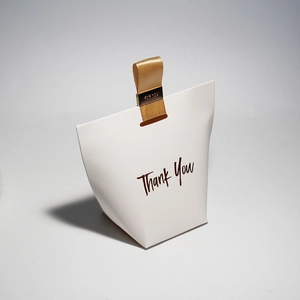 Close-up of a white trapezoid gift box featuring a gold Thank You script and ribbon