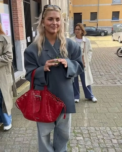 Detail of oversized grey blazer jacket worn with a vibrant red leather handbag on street