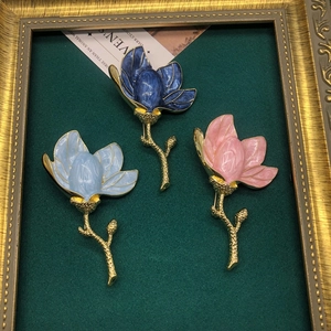 Close-up of enamel magnolia brooches in blue and pink with gold-plated alloy details