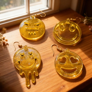 Close-up of yellow resin rabbit and smiley face earrings on a sunny wooden windowsill